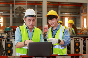 Asian male Hard Hat chief engineer using laptop to train workers to check checks heavy metal machinery