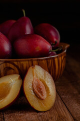 Fototapeta na wymiar Sliced plums with stone and brown bowl withviolet plums on a wooden table. Side view.