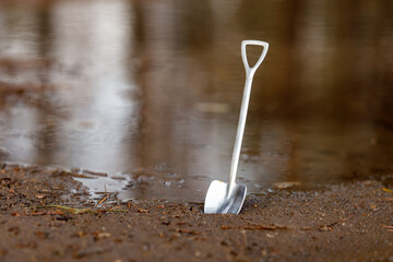 shiny steel shovel by the pond, water and mud
