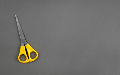 Yellow scissors lie on a gray background with the texture of thick paper