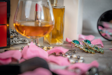 verre de bourbon sur une table de maquillage avec des boucles d'oreille, des pétales de roses et du parfum