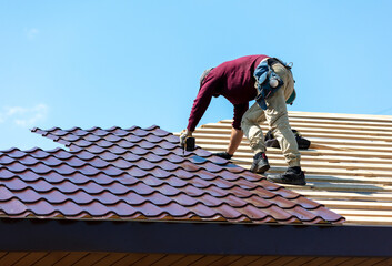 Workers install metal roofing on the wooden roof of a house.