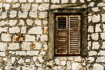Fototapeta na wymiar Stone wall and window with closed wooden shutters