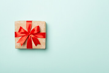 Gift box with red ribbon bow on color background, top view