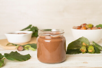 Hazelnut cream with nuts and green leaves on wooden table