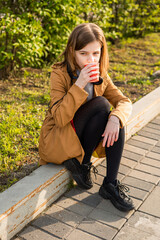 A teenage girl on the street sits on the edge of the road a glass of coffee in her hand. High quality photo