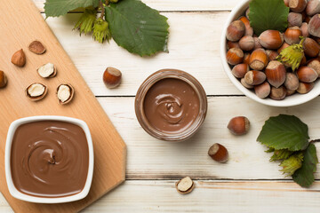 Hazelnut cream with nuts and green leaves on wooden background, top view