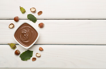 Hazelnut cream with nuts and green leaves on wooden background, top view