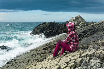 traveler sits on the shore of a stormy sea, on a natural pavement made of columnar granite