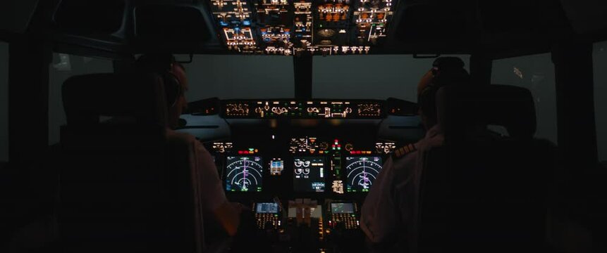 Commercial aircraft pilots performing pre flight check of the jet airplane at night. View from inside the cabin. Real aircraft, nighttime shot