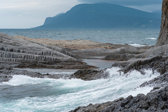 severe rocky seashore formed by columnar basalt against the backdrop of a stormy sea, coastal landscape of the Kuril Islands