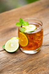 Glass of ice tea with lime slice with mint on wooden table