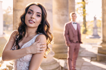 Happy bride and groom are standing apart from each other near the columns of the building