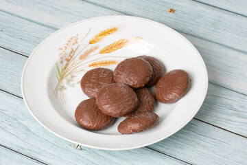 Pão de mel coberto com chocolate em um prato branco decorado, em uma superficie de madeira