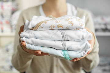 Baby clothes in female hands. Set of beautiful baby bodysuits. Preparation before childbirth.