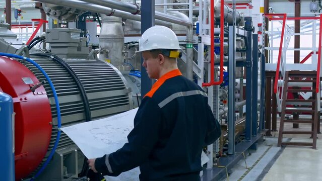 A young engineer at a factory checks the blueprint of a pipeline connection to a compressor unit. An electrical engineer checks the connection of an industrial electric motor according to the scheme.