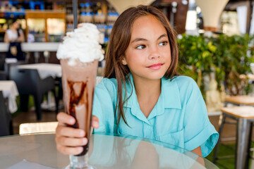 Beautiful child kid girl eating a chocolate shake in a restaurant. Cold summer desserts for kids....