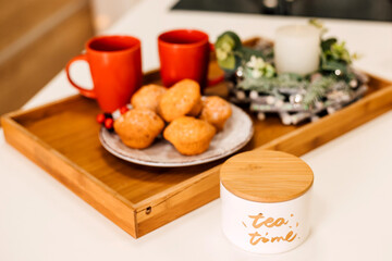 On the table is a plate of muffins, two red cups and a candle. New Year