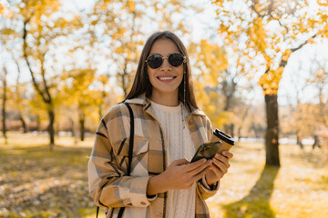 attractive young woman walking in autumn wearing jacket using phone