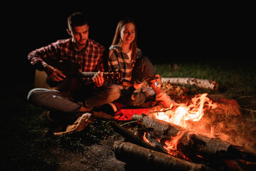 Young couple in love on romantic date at evening playing on guitar by the fire.