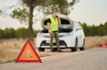emergency triangles signaling a car breakdown and a man calling car insurance for assistance