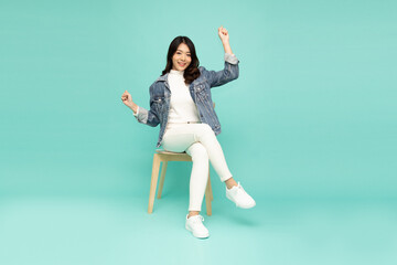 Fototapeta na wymiar Attractive beautiful Asian woman sitting on white modern chair and hands up raised arms from happiness, Full body composition