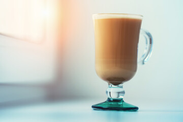 Full glass of cappuccino standing on white window sill at early morning close up view
