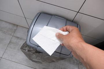 Human hand holding and throwing away a tissue, toilet paper to a bin in restroom