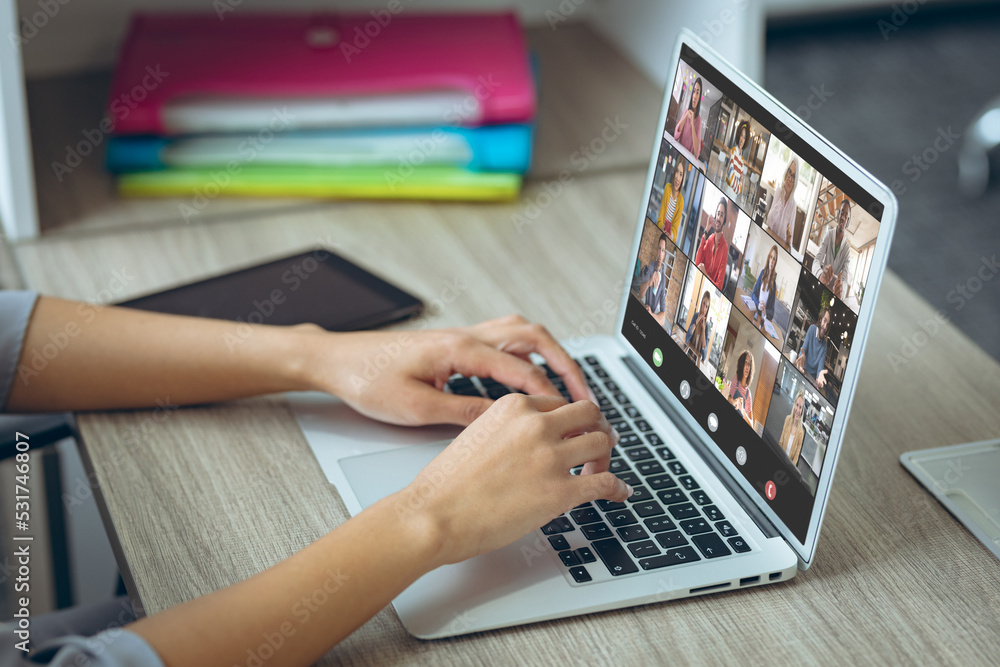 Wall mural Cropped hands of caucasian woman on video conference with coworkers over laptop in office