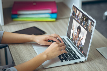 Fototapeta premium Cropped hands of caucasian woman tying on keyboard while discussing with coworkers over laptop