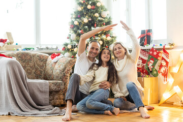 Beautiful young family enjoying their holiday time together, decorating Christmas tree, arranging the christmas lights and having fun.