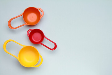Colorful plastic measuring spoons and measuring cups on bright background top view with space for text