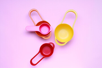 Colorful plastic measuring spoons and measuring cups on bright background top view