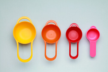 Colorful plastic measuring spoons and measuring cups on bright background top view