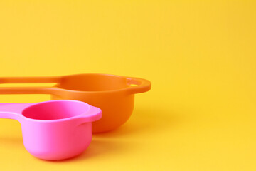 Colorful plastic measuring spoons and measuring cups on bright background with space for text