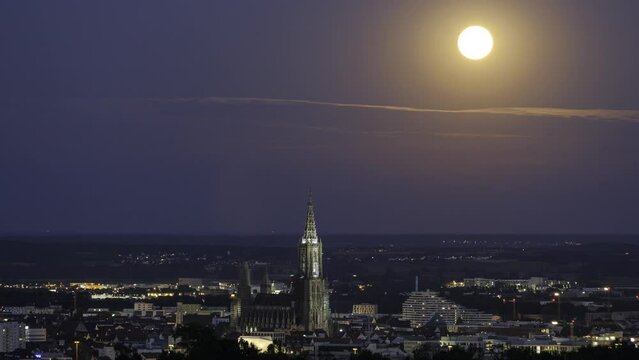 Time lapse shot of full moon rising behind clouds above cities of Ulm and New-Ulm (Neu-Ulm) at dusk