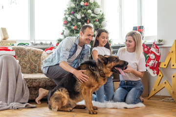 Merry Christmas and Happy New Year. Happy family with dog are waiting for the New Yearwhile sitting near beautiful Christmas tree at home.