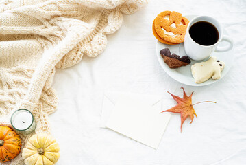 Blank greeting card mockup whit cup of coffee and cookies. Autumn, fall, halloween concept. Pumpkins and candle on white woolen plaid with decorations