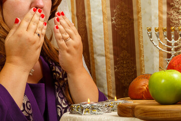 A Jewish woman in a veil falling from her hair reads a blessing on the candles covering her face...