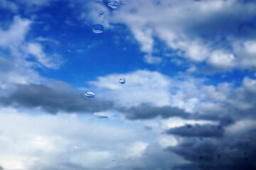 Fototapeta na wymiar Glasscheibe mit Regentropfen vor blauem Himmel mit grau-weißem Wolkengebilde bei Regen am Nachmittag im Herbst