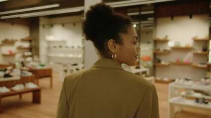 A stylish African-American woman in a jacket walks into a luxury shoe store