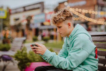 Teen boy using smartphone sitting on the street. Social media concept