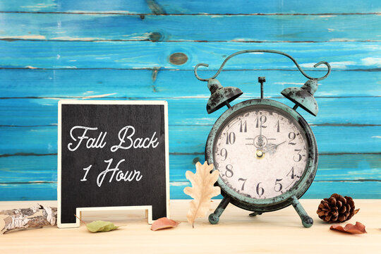 Image of autumn Time Change. Fall back concept. Dry leaves and vintage alarm Clock on rustic wooden table