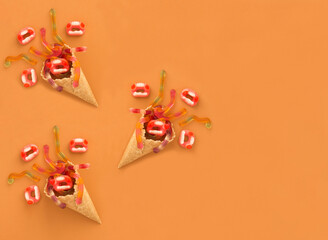 Ice cream cone with candy for Halloween on the orange background. Top view. Copy space.