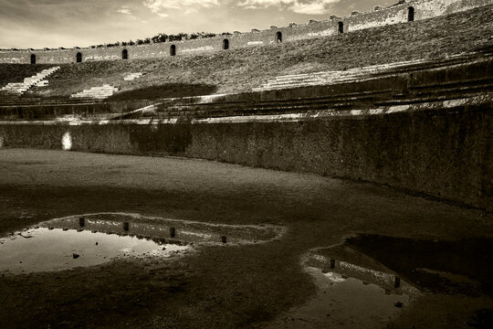Amphitheatre of Pompeii after rain. Beautiful reflection in water paddles. Sightseeing, travel, heritage,  culture concepts. Pompeii archaeological park, Italy tourist attraction. Sepia historic photo