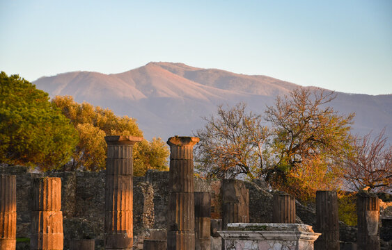 Pompeii archaeological park. Sunset view  of temple columns and mountains at background touched with golden sunlight. Sightseeing, travel, heritage and culture concepts. Italy tourist attraction.