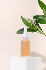 Obraz na płótnie Canvas Mockup cosmetics serum with a pipette in a transparent frosted glass and orange liquid. Facial peeling with lactic Aha acid on a white cubic pedestal, beige background with leaves