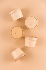 Vertical composition with brown paper food containers for soup or ice cream, cup with paper cap over light brown background, mockup image. Sustainable food packaging. Monochrome