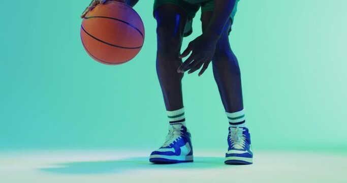 Video of low section of african american male basketball player bouncing ball on blue background