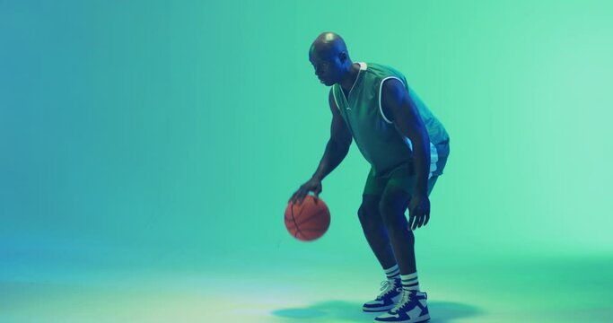 Video of african american male basketball player bouncing ball on blue background